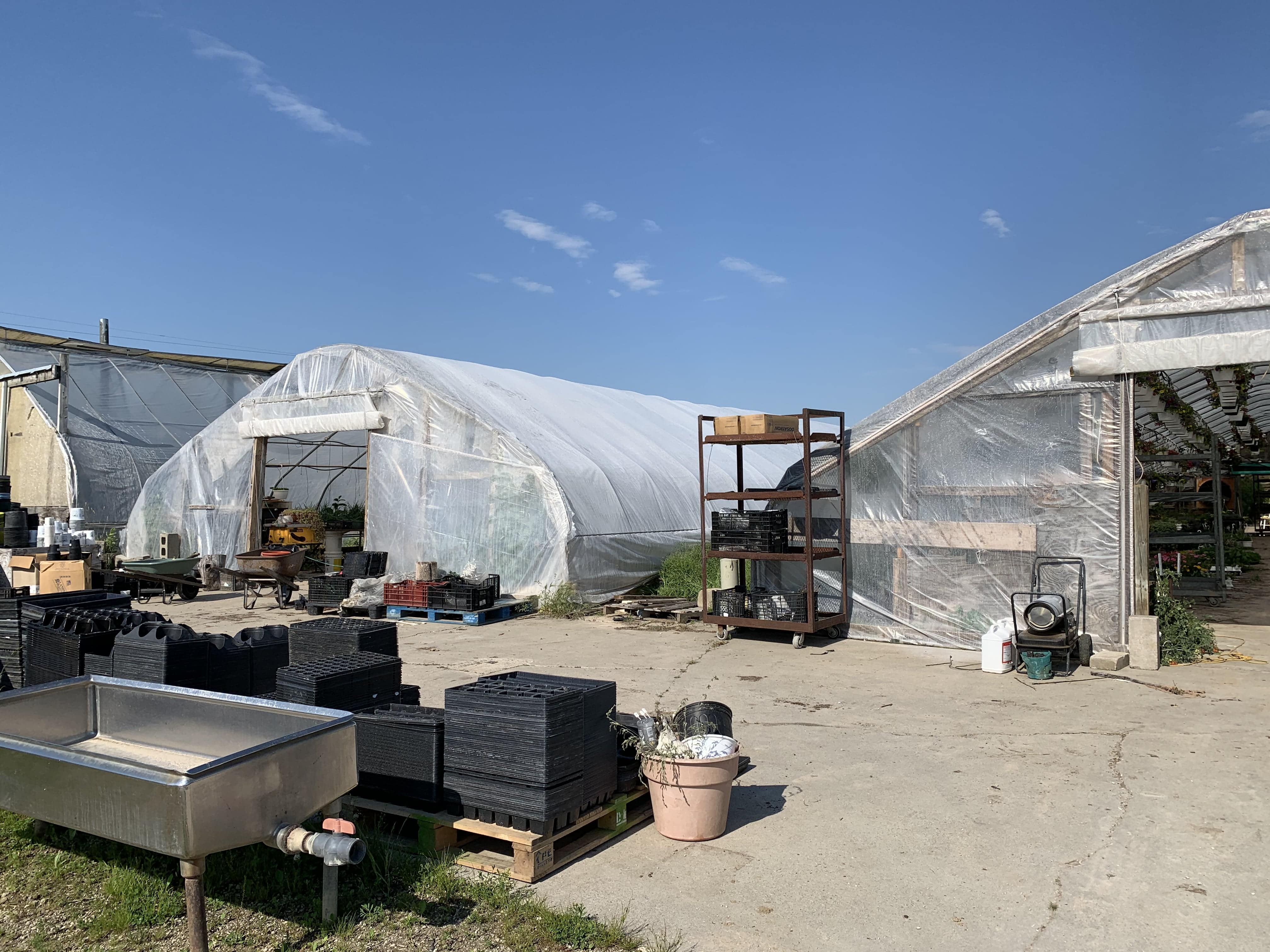 2 greenhouses with plants & equipment in front.